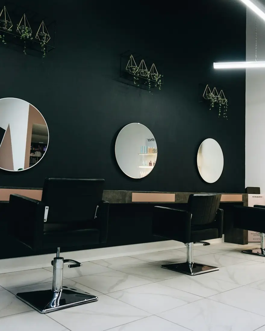 Interior de una peluquería con sillones negros y espejos redondos, foto de ejemplo